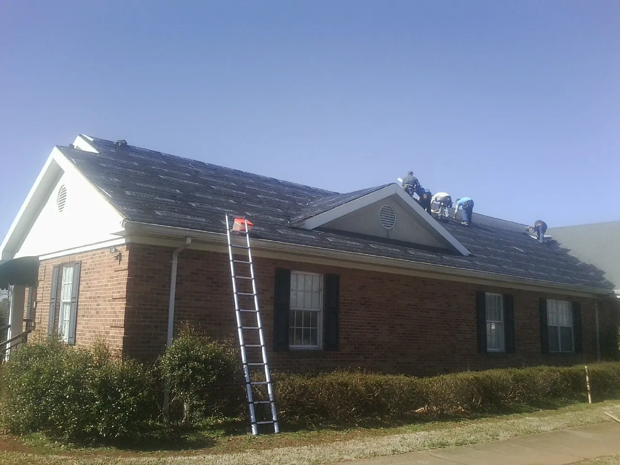 Crew tearing shingles off a brick ranch roof with a ladder set — Emergency Roof Repair work by our crew in Steep Falls