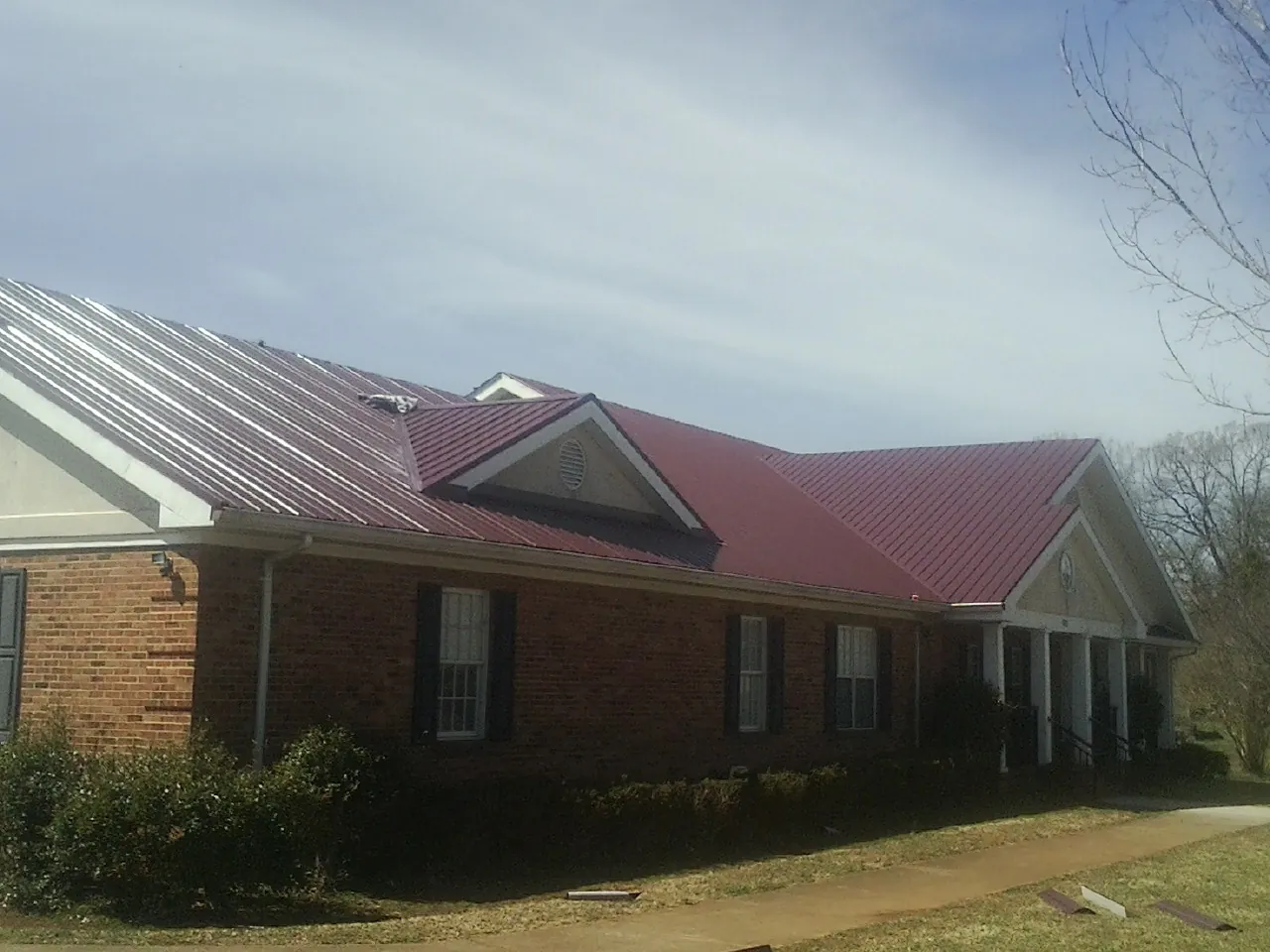 Red metal roof with gabled entries on a long brick building, from a Hail Damage Roof Repair job in Steep Falls