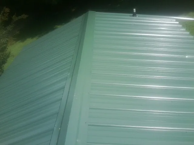 New green metal panels meeting at the ridge of a roof — Flat Roof Repair work by our crew in Steep Falls