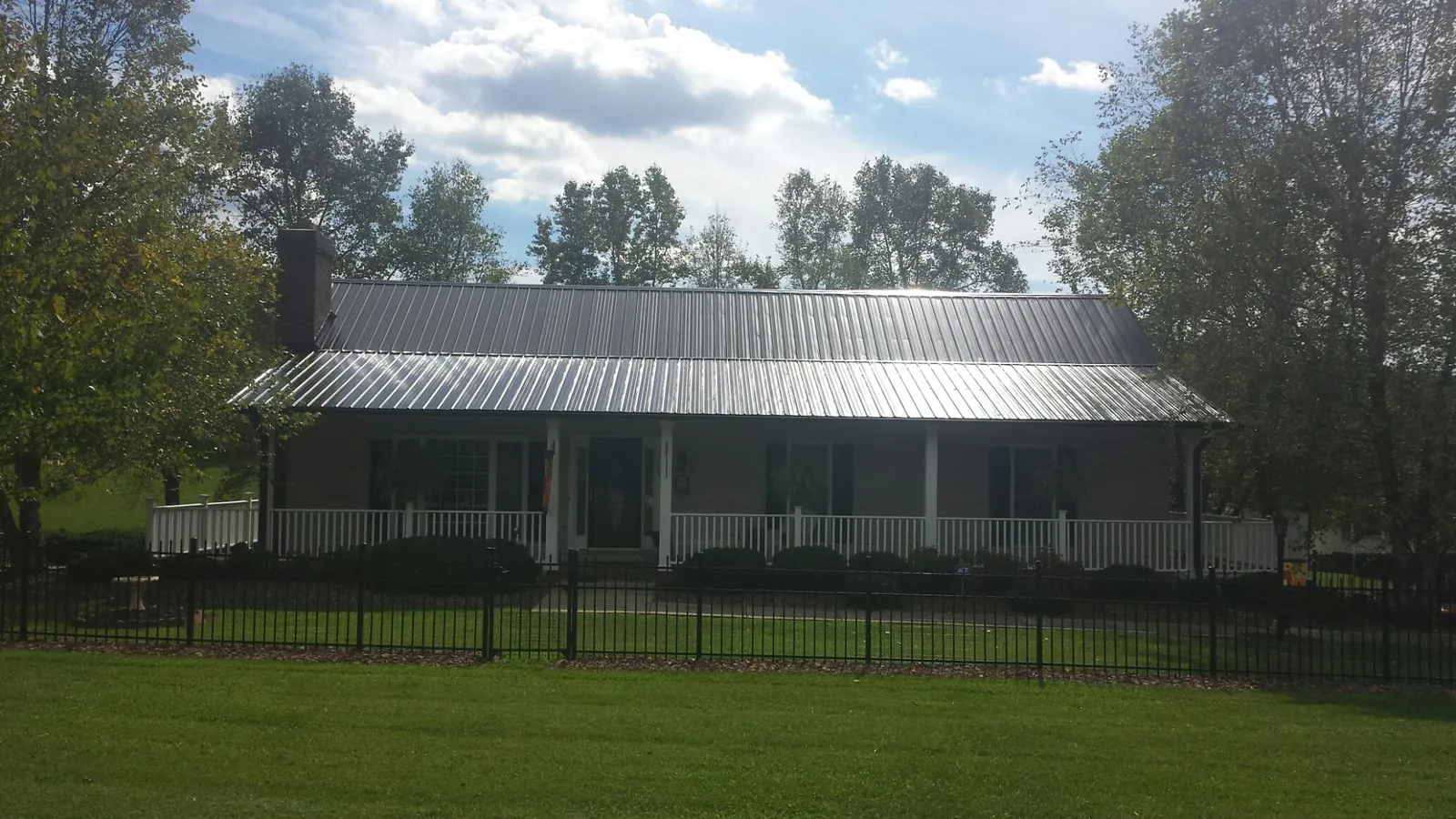 Gray metal roof on a brick ranch with a full width front porch — Gutter Guard Installation work by our crew in Steep Falls