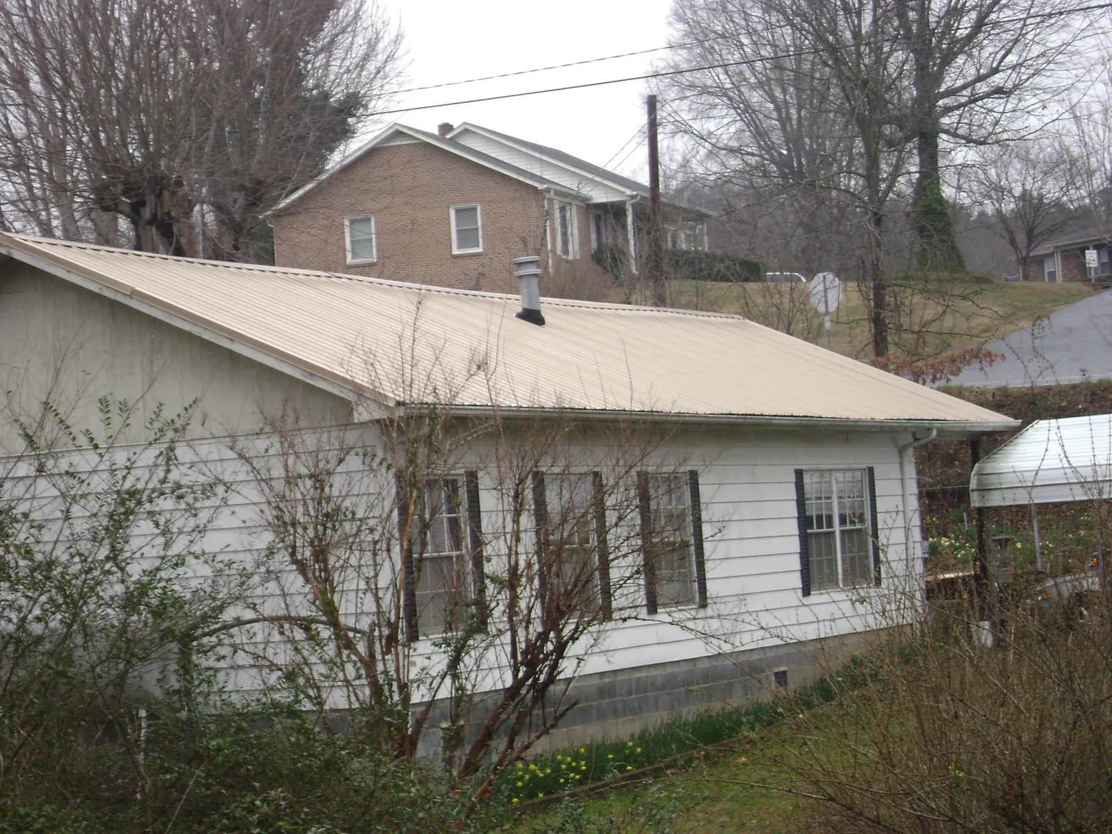 Tan metal roof on a white sided house set into a hillside — Commercial Roofing by Roofing Brothers in Steep Falls