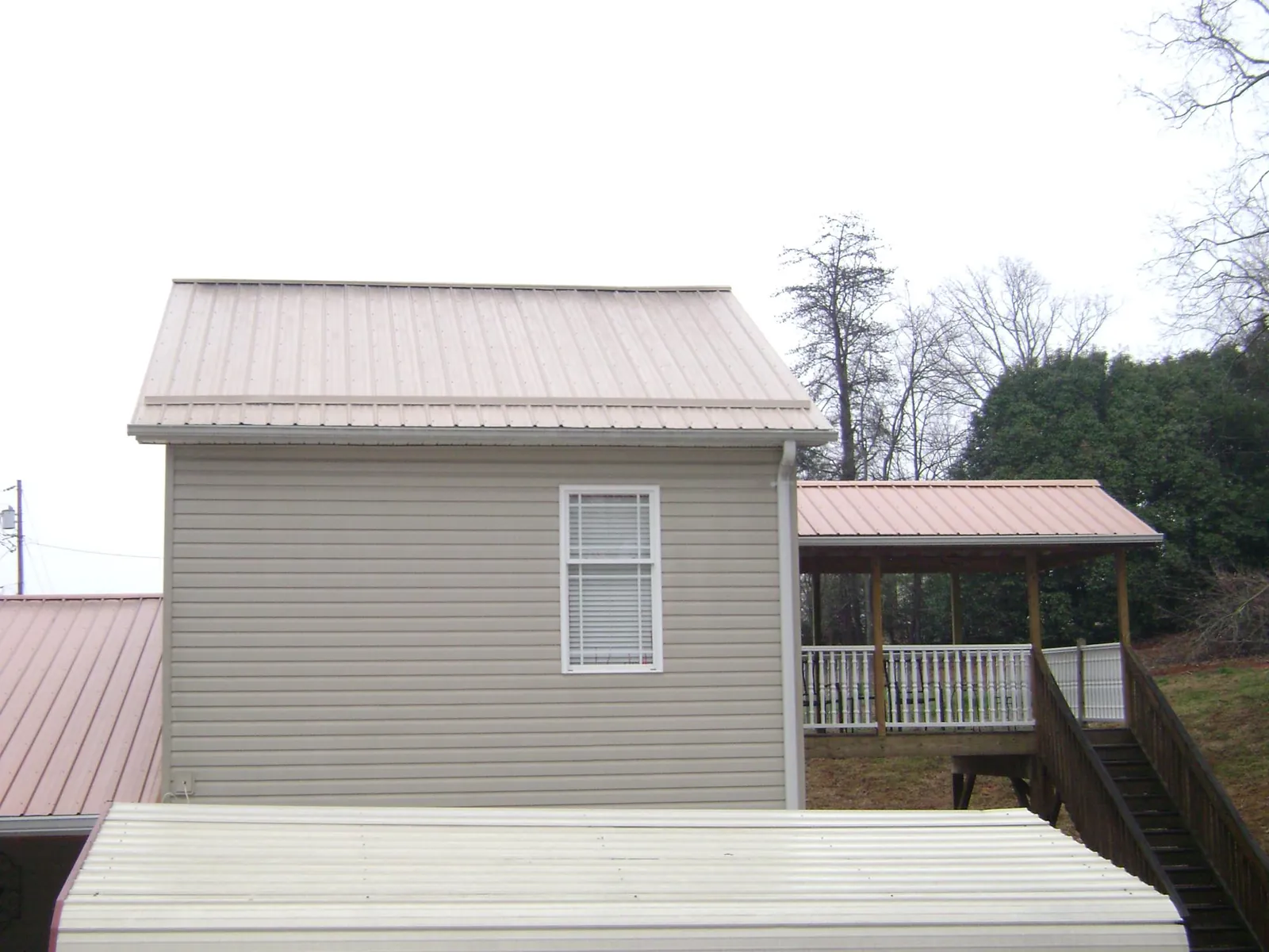 Tan metal roofs on a two story addition and attached porch, from a Roof Replacement job in Steep Falls